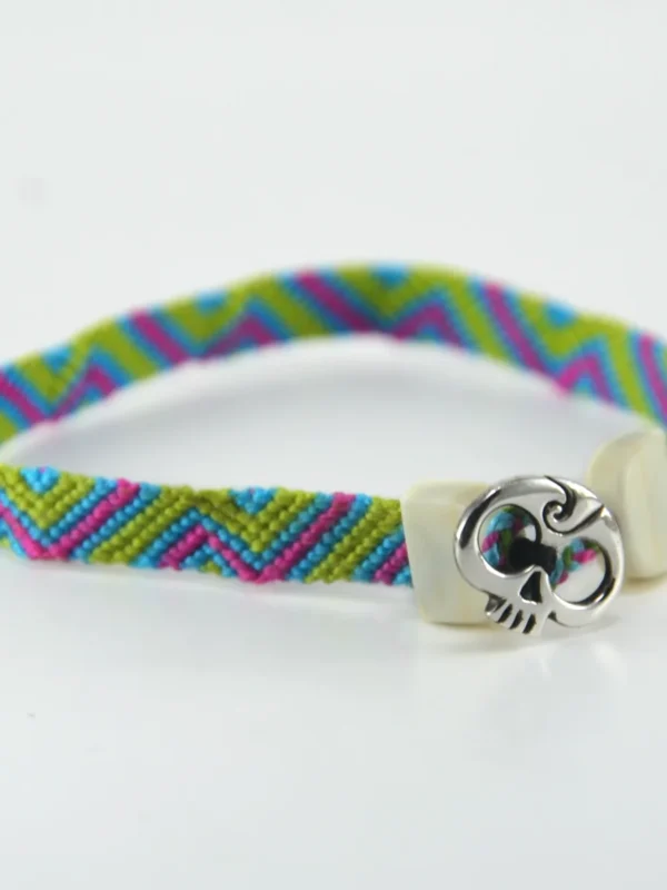 Esta **pulsera macrame multicolor** y plata ley 925 destaca por el contraste dinámico de sus tonos y la combinación impecable de materiales. Diseñada y elaborada artesanalmente por Santiago Rugeles, es una joya contemporánea concebida para brindar frescura y personalidad a cualquier estilo. El tejido de esta **pulsera macrame multicolor** resalta por su patrón geométrico en verde manzana, fucsia y azul turquesa, rematado con terminales esculpidas en hueso de res y un distintivo aplique frontal de calavera forjado en plata 925. --- ### Detalles y Especificaciones: * **Materiales:** Hilos de algodón de alta resistencia, aplique central en plata ley 925 y terminales en hueso de res. * **Proceso:** Tejido a mano y ensamblado artesanal, garantizando acabados definidos y durabilidad. * **Estilo:** Unisex / Joyería contemporánea de autor. --- ### Cuidado de tu pieza: Para conservar la viveza de los colores del algodón y el brillo de la plata 925, evita el contacto con perfumes, cremas o lavar la joya con detergentes agresivos.